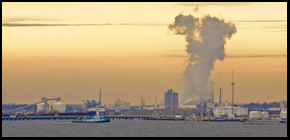 Image of a port with boats in the water and smoke billowing up in the distance.