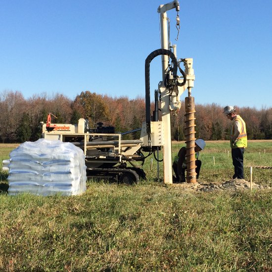 Two people with hardhats, and digging equipment in a field