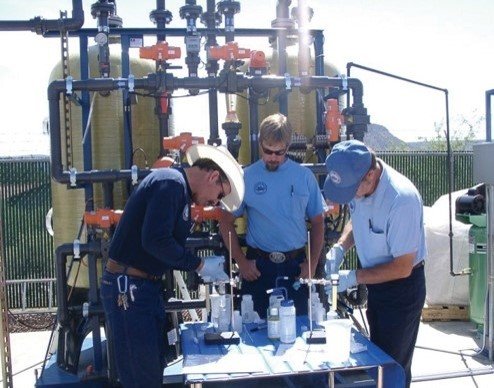 Three researchers stand around a table during the arsenic treatment technology demo program.