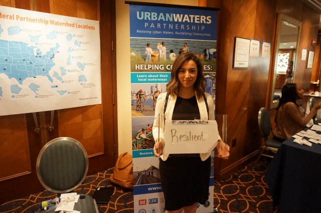 girl holding sign that says resilience in front of urban waters banner