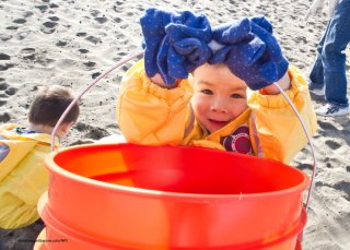 Child helps clean up a beach by carrying a bucket for collecting trash.