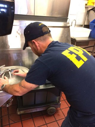 a man in an EPA shirt holds a small vial under running tap water