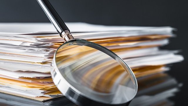 Image of a magnifying glass leaning against a stack of papers.