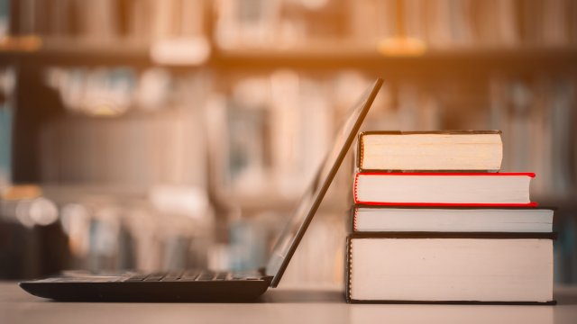 Laptop with stack of books on top of table in the library referencing standards development.