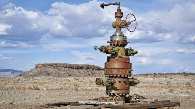 Abandoned wellhead pictured in the middle of the desert with sky in the background