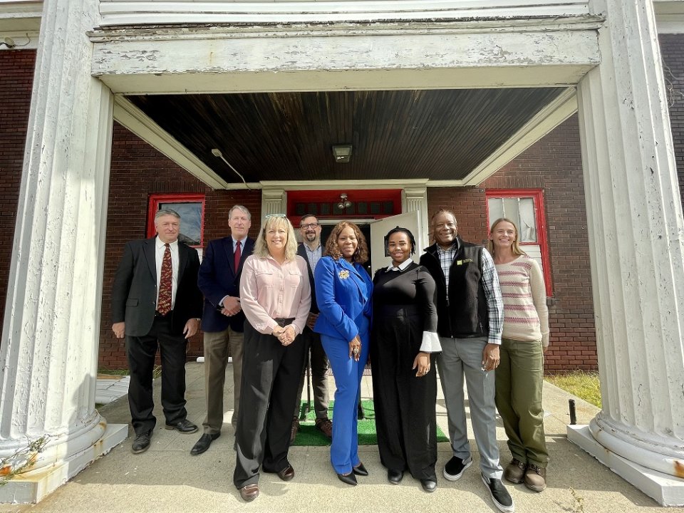 People are seen standing in a group smiling in front of a building.