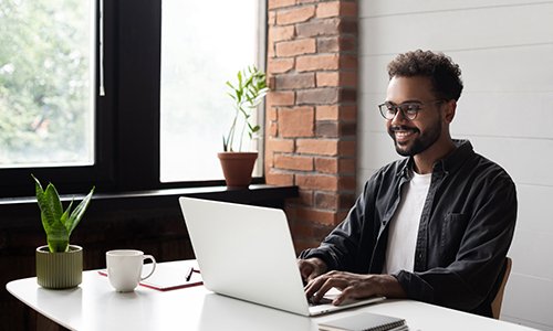 Photo of a man who is smiling while typing on his laptop.