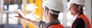 This is a photo of two men with hard hats on talking at a construction site.