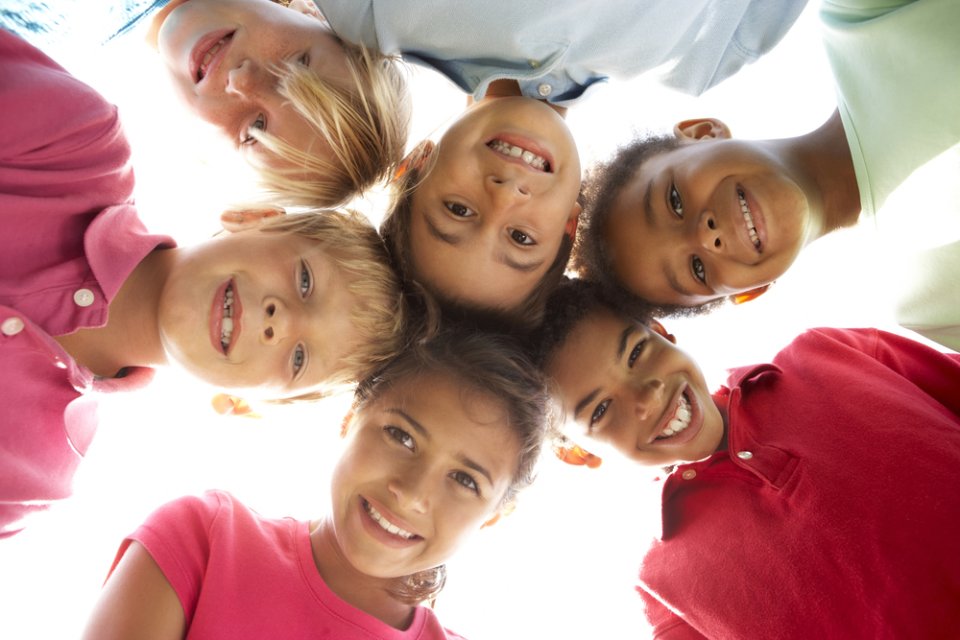 A group of children standing shoulder-to-shoulder and looking down into the camera lens 