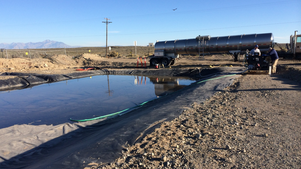 A large tanker truck in the background of a holding lagoon filled with water.