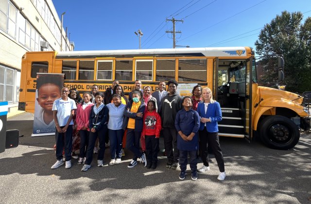 Students in front of electric school bus smiling.