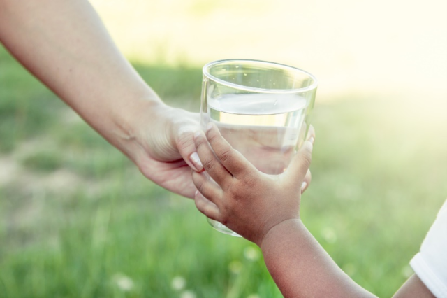 Adult handing a child a glass of water.