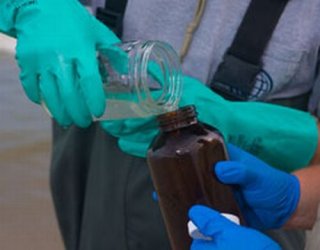 Photo showing a scientist pouring a solution from one container to another for testing.