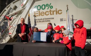 Administrator Regan with school children with signed order in front of electric trash truck