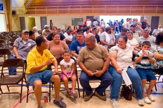 This is a photo of people sitting in a gym for a public meeting