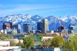 Salt Lake City skyline with mountains and blue sky in the background and trees in the foreground. 