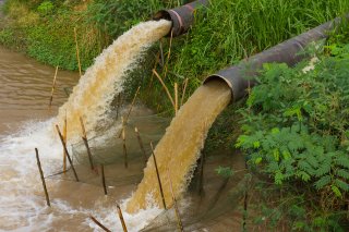 Two pipes dumping wastewater into river.