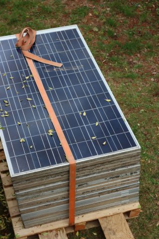 This is a close-up of stack of solar panels bundled together with a strap and lying outside on grass