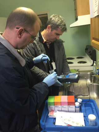 Two researchers in a residential kitchen analyzing disinfection residuals in tap water.