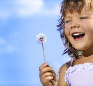 Young girl smiles as she prepares to blow on a seeded dandelion