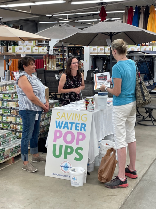 Photo of three women at a table with a sign that says "Saving Water Pop Ups"