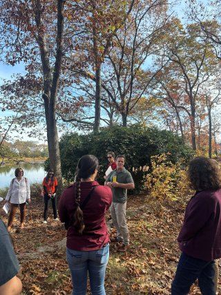 People listen to a presentation in a forested area.