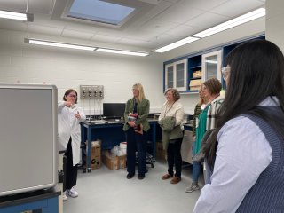 People gather around a scientist showing a sample.