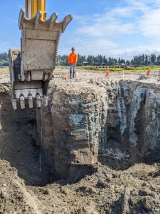 Excavator shown digging large hole revealing solidification of soil and contamination after mixing with cement.