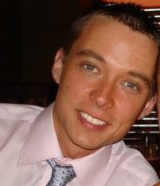 A close up of a man in a light shirt and blue tie. He is smiling.