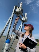 A scientist stands outside inspecting the wiring on an SPod air sensor